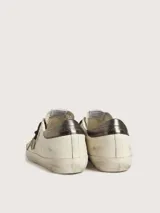 Zapatillas Golden Goose modelo Super-Star, de cuero color blanco envejecido con estrella de glitter verde y detalles en cuero color negro en el talón. Cordones marrones y suela de goma.