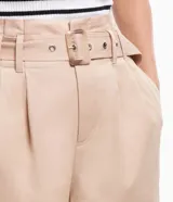 Pantalón pantacourt color beige, confeccionado en tricolina. Presenta cintura clochard con trabillas, pliegues delanteros y bolsillos laterales. Incluye cinturón con hebilla rectangular con estampado carey.