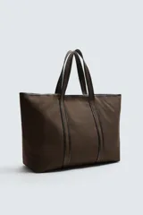 Bolso tipo shopper color marrón, fabricado en tejido de algodón con detalles en piel. Asas fabricadas en piel y algodón. Compartimento principal con cierre mediante imán. El interior cuenta con un bolsillo con cierre mediante cremallera y un bolsillo plano.