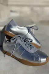 Zapatillas deportivas plateadas con detalles en gamuza gris y suela de goma color caramelo.