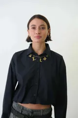 Camisa corta negra de corte holgado, abotonada al frente y con cuello camisero.