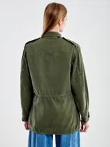 Chaqueta militar verde oliva de algodón con cuello camisero, cierre frontal con botones y cuatro bolsillos delanteros con solapa. Decorada con apliques metálicos y parches de tela.