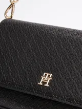 Cartera de hombro negra con diseño integral del monograma TH en bajo relieve y piezas metálicas pulidas. Tiene asa extraíble y correa ajustable y extraíble, cierre a presión en la solapa, un compartimento principal y bolsillo interior con cremallera.