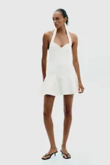 Vestido corto blanco de tejido de punto elástico, con cuello halter, escote corazón y cierre con botones en el cuello.