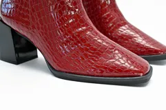 Bota de charol brillante texturado color burdeos, con diseño que cubre el tobillo y taco geométrico de 7 cm.