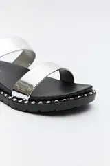 Sandalias planas plateadas con dos tiras anchas y suela negra con detalles metálicos.