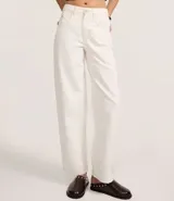 Pantalón baggy de tiro medio color blanco, confeccionado en sarga de algodón. Cuenta con trabillas en la cintura, cuatro bolsillos, cierre con cremallera, lateral desplazado y costuras contrastantes.