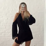 Vestido corto negro con escote halter, hombros descubiertos y mangas largas acampanadas.