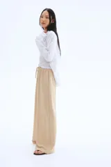 Pantalón de punto color beige, de corte holgado con piernas amplias, tiro alto, cintura elástica y cordón para ajustar.
