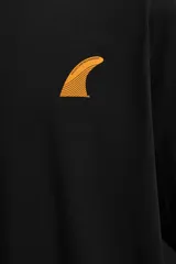 Camiseta negra de algodón con calce relaxed fit, cuello redondo y manga corta. Estampado pequeño en el pecho con la silueta de una quilla de tabla de surf color naranja.