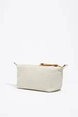 Neceser mediano de nylon color crudo, con estructura blanda, cierre de cremallera, tirador de cordón, logo metálico y acabados dorados.