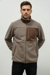 Campera de poliéster color beige con cuello alto y cierre frontal. Presenta detalles en color marrón oscuro en el cuello, un bolsillo vertical con cierre en el pecho y ribetes en los bolsillos laterales.