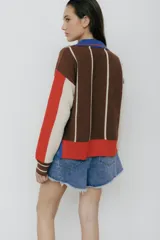 Buzo tipo polo de punto con rayas verticales en tonos beige, marrón y rosa. Tiene cuello polo marrón, cierre parcial con botones amarillos y terminaciones acanaladas en puños y ruedo.