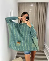 Sweater tejido de punto color fucsia con diseño de trenzas verticales en color naranja. Tiene cuello redondo y dos bolsillos frontales.