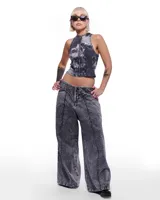 Pantalón de denim gris con lavado artesanal, corte sastrero de pierna ancha, tiro alto y pretina cruzada.