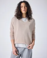 Sweater de cachemir color beige, con cuello en V, corte oversize, mangas largas, hombros caídos y terminaciones acanaladas.