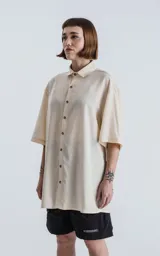 Camisa de manga corta color off-white, con cuello camisero y botones frontales marrones. Corte holgado.