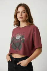 Remera cropped color borgoña de algodón, con cuello redondo y mangas cortas. Estampado frontal con un corazón sagrado con llamas, rosas y la leyenda 'Love Blooms'.