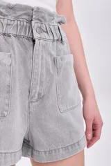 Short de jean gris con cintura paper bag, elástica y con botón. Tiene bolsillos delanteros y traseros.