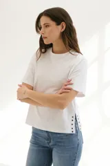 Remera blanca de algodón de corte recto, con cuello redondo y mangas cortas. Presenta detalle de aberturas laterales con ojales metálicos.
