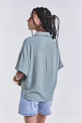 Camisa verde agua con cuello clásico, cierre frontal con botones, mangas cortas con dobladillo y dos bolsillos de parche en el pecho.
