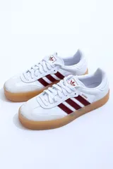 Zapatillas Adidas Samba de cuero blanco con puntera de gamuza gris y tres tiras de cuero bordó. Suela de goma color caramelo traslúcida.