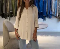 Camisa beige de lino, de corte recto y manga larga con puños arremangados. Tiene cuello camisero, cierre frontal con botones de coco y aberturas laterales.