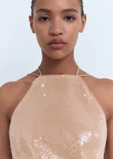 Vestido midi color beige, con diseño recto y escote halter con cierre de lazo en la espalda. El tejido principal es de lentejuelas.