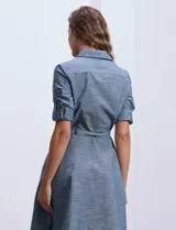 Vestido camisero blanco de algodón con cuello con solapa, delantera abotonada, mangas 3/4 regulables con presilla y botón, y cintura con lazo de ajuste.