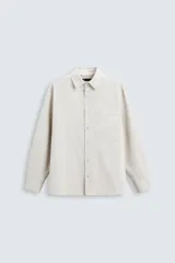 Camisa color crema de corte relaxed fit, confeccionada en tejido de mezcla de algodón suave al tacto. Cuenta con cuello solapa, manga larga con puños abotonados, bolsillo de parche en el pecho y cierre frontal con botones.
