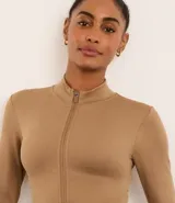 Campera deportiva color beige, de corte ajustado, confeccionada en tejido de poliamida seamless con textura acanalada y cuello alto. Posee cierre delantero por cremallera y mangas largas.