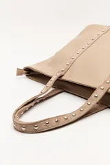 Bolso shopper de símil cuero color beige, con asas largas decoradas con tachas metálicas.