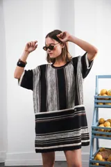 Vestido corto tejido con rayas verticales en tonos negro, gris y marrón. Tiene cuello redondo y mangas cortas.