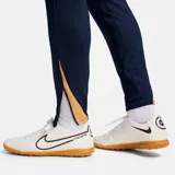 Pantalón largo de fútbol Nike FC Barcelona Strike para hombre, color azul marino con detalles en naranja. Presenta el escudo del club y el logo de Nike bordados.