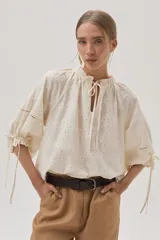 Blusa color crudo con bordado calado, cuello con volantes y lazos para ajustar. Mangas abullonadas con puños elásticos y lazos.