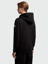 Buzo negro con capucha y cierre frontal completo. Presenta un bolsillo tipo parche en el pecho confeccionado en tejido técnico.