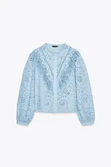 Camisa celeste de cuello redondo y manga larga, con bordados perforados y volantes. Cierre frontal con botones ocultos por solapa.