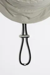 Gorro tipo bucket color gris topo de tejido técnico con cordón ajustable y etiqueta de silicona con el logo de Bimba y Lola.