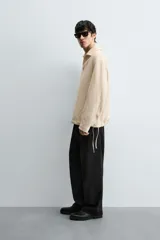 Pantalón negro de corte relajado y pierna ancha, confeccionado en mezcla de algodón y lino. Presenta cintura elástica ajustable con cordón y cierre frontal con cremallera y botón.