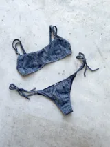 Conjunto de bikini con estampado a cuadros azul y blanco, compuesto por un corpiño bandeau con breteles regulables y una bombacha vedetina con tiras laterales para atar.