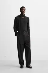 Pantalón negro de corte amplio, con pliegues frontales, bolsillos laterales y traseros de ojal. Incluye cinturón de la misma tela con hebilla metálica.
