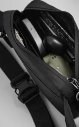 Riñonera negra de material impermeable (tracker waterproof) con tres bolsillos frontales con cierre y un bolsillo lateral. Incluye correa regulable con broche de mochila.