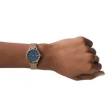 Reloj Skagen con caja redonda de acero color oro rosa, dial azul y malla milanesa dorada.