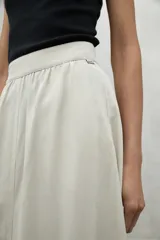 Falda midi color crema, de corte evasé, con cintura elastizada, bolsillos laterales y aberturas frontales y traseras.
