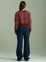 Cardigan de punto color borgoña con diseño geométrico en blanco y detalles en azul. Tiene cuello redondo, cierre frontal con botones rojos y mangas largas con puños acanalados.