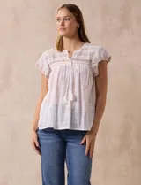 Blusa blanca de algodón con cuello a la base y escote en V con lazo de ajuste. Tiene mangas cortas con terminación amplia y bordados en delantera, mangas y espalda.