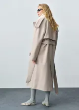 Trench color beige con solapas, trabillas en los hombros y puños, cinturón desmontable y bolsillos laterales.