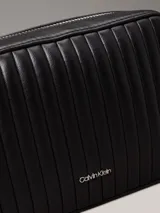 Cartera bandolera Calvin Klein negra con diseño acolchado de líneas verticales, correa de cadena plateada, cierre superior con cremallera y logo metálico frontal.