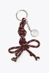 Accesorio charm para bolso con cuerda anudada en tonos borgoña, azul y beige, con abalorios metálicos plateados.
