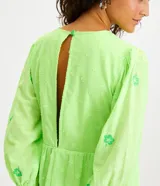Vestido corto color verde lima con estampado de flores en verde claro, escote en V con lazo, mangas 3/4 con puños elásticos y falda con volantes.